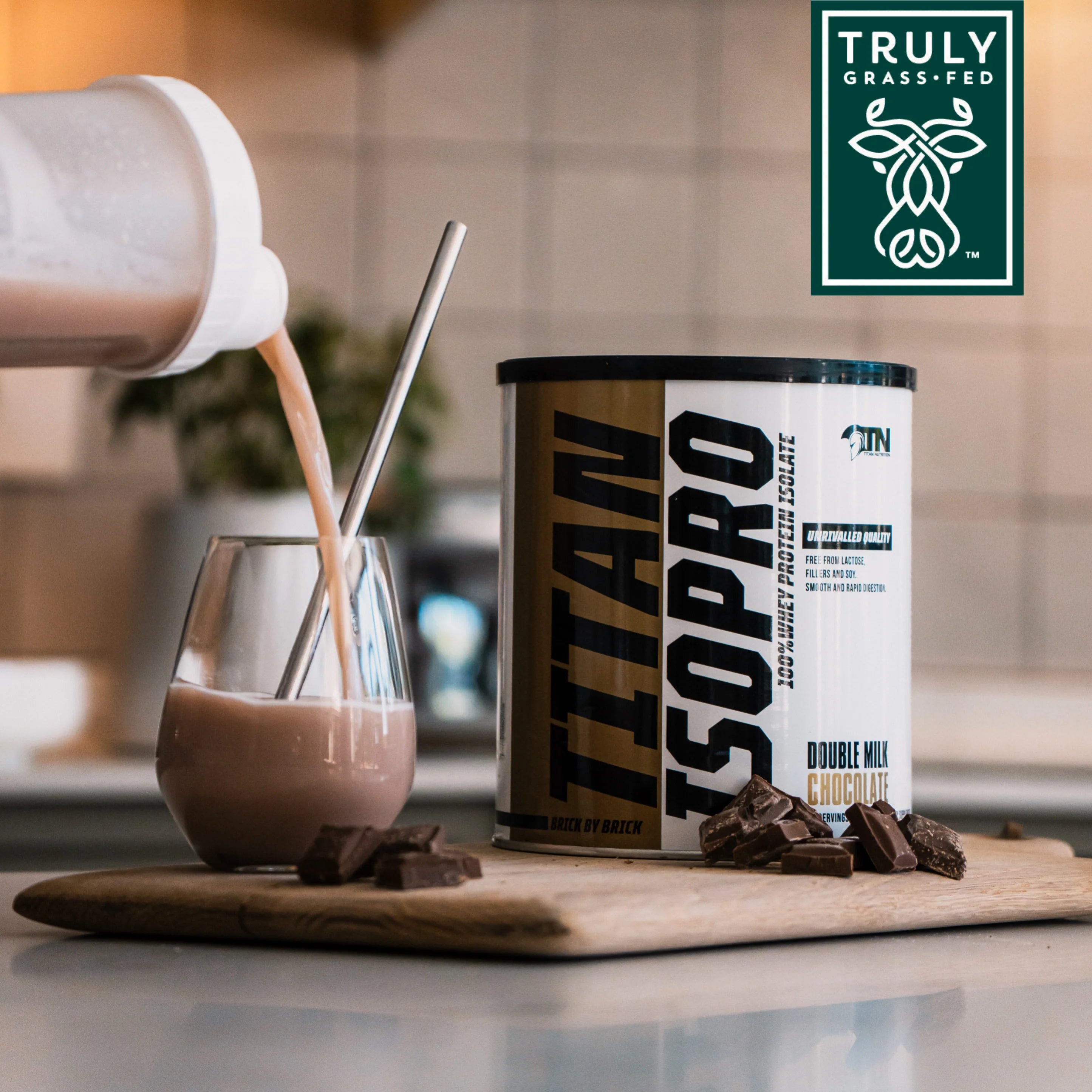 Titan Isopro Double Milk Chocolate supplement can with a glass of chocolate milk on a wooden board, featuring the Truly Grass-Fed logo. Muscle Mecca