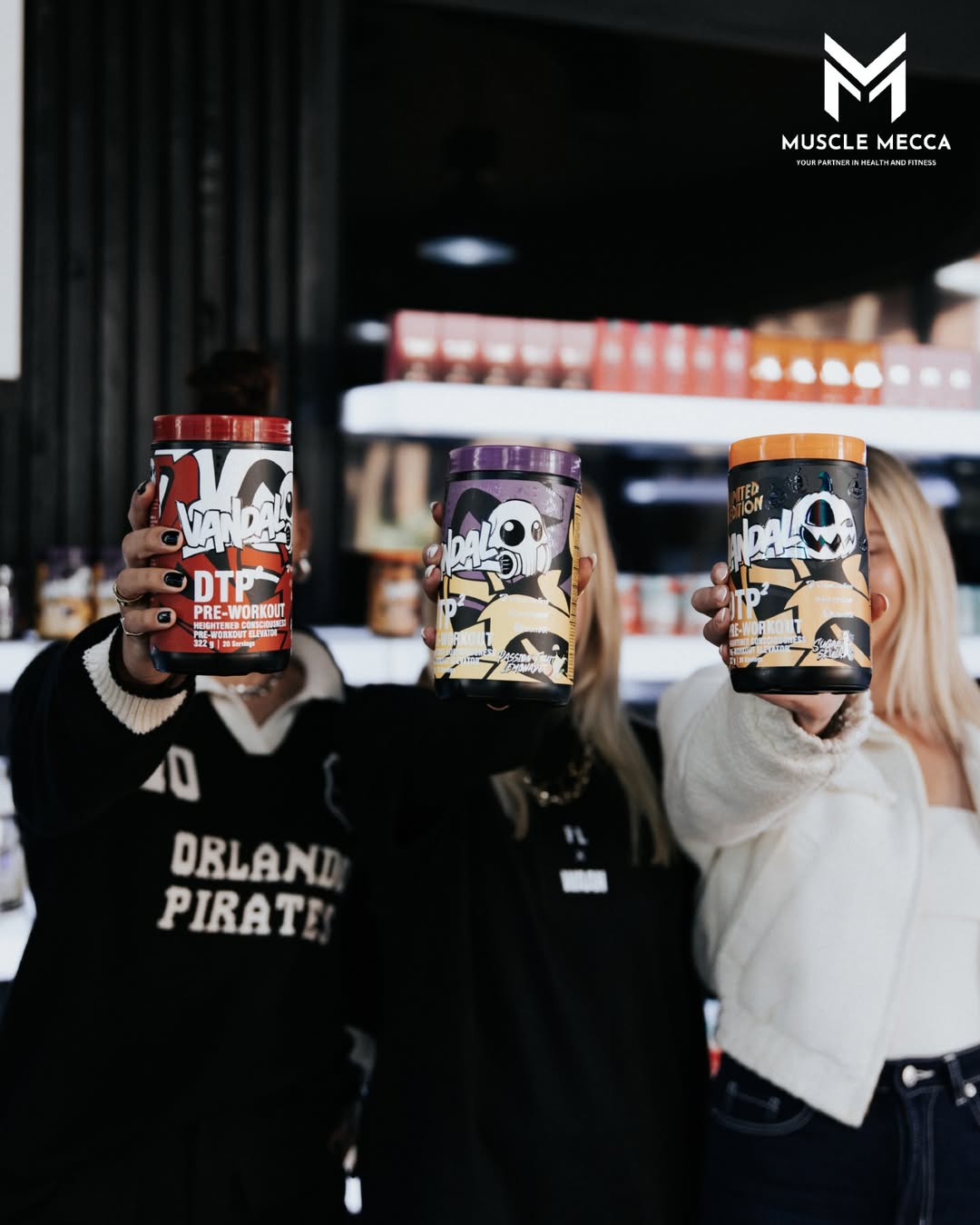Three people holding containers of Muscle Mecca products in a store setting.