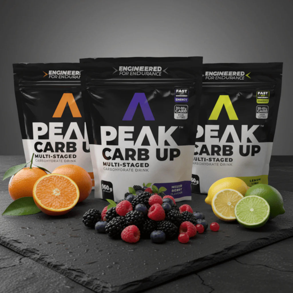 Three packages of Peak Carb Up with fruits and oranges on a dark surface Muscle Mecca