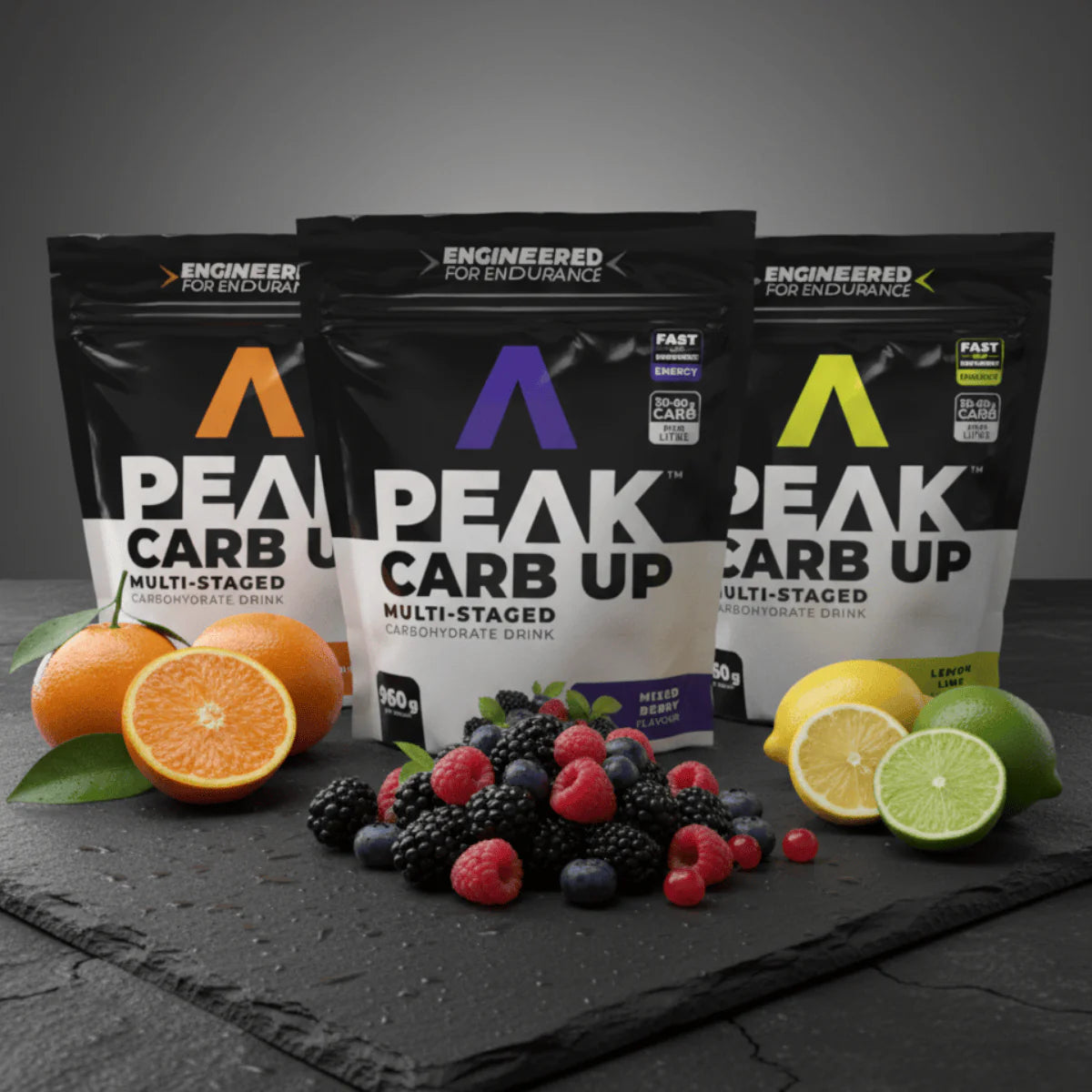 Three packages of Peak Carb Up with fruits and oranges on a dark surface Muscle Mecca
